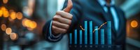 Business professional showing thumbs up gesture next to glowing blue financial chart with upward trend against blurred bokeh background, representing success and growth.