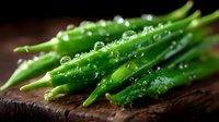 Fresh green asparagus spears with water droplets on dark wooden surface in dramatic lighting, macro food photography highlighting texture and freshness.