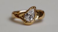 Elegant pear-shaped diamond engagement ring in yellow gold setting with organic flowing design and unique asymmetrical band, showcasing modern luxury jewelry craftsmanship.