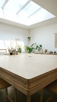 Bright minimalist workspace with wooden desk, skylight windows, potted plants, and natural light for creative studio or home office design.