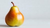 Fresh ripe pear with yellow and red blush skin on light background, close up view of whole fruit with stem showing natural organic produce.