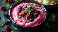 Fresh berry smoothie bowl topped with raspberries, blueberries, chia seeds and mint leaves in dark ceramic bowl, healthy breakfast or dessert concept.