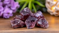 Raw purple fluorite crystal chunks on wooden surface with soft floral background, showcasing natural mineral formation and metaphysical properties for wellness decor.