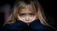 Young blonde girl with striking blue eyes peering over dark knit sweater, expressing innocence and vulnerability against dark background. Emotional portrait captures childhood contemplation.