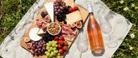 Overhead view of charcuterie board with cured meats, cheese, grapes, nuts and rosé wine on linen cloth for picnic entertaining and outdoor dining occasions.