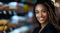 Young African American businesswoman with braided hair smiling confidently in modern office environment for professional corporate marketing materials.