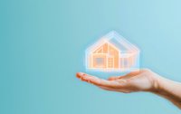 Female hand holding glowing holographic house icon on turquoise background, representing smart home technology, real estate, or property protection services.