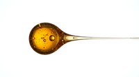 Golden amber liquid in glass spoon with long handle, isolated on white background, suitable for cooking, medicine, and design projects.