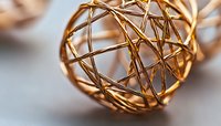 Decorative golden wire sphere made of thin metal strands intertwined in abstract geometric pattern, macro photography with soft blur background.