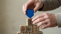 Senior hands placing blue wooden block on stack of security-themed blocks representing cybersecurity protection and data safety concepts for business.