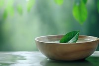 Wooden bowl with green leaf floating on water against blurred natural background for spa, wellness, and meditation concepts.