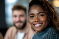 Young African American woman with bright genuine smile wearing teal sweater, natural curly hair, radiating positive energy and confidence in casual indoor setting.
