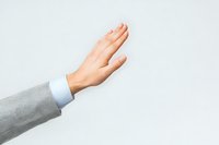 Professional hand gesture showing stop or high five motion against light background, wearing formal grey suit sleeve and white shirt cuff.
