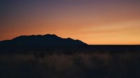 Desert mountain silhouette against vibrant orange and purple sunset sky with golden hour lighting over arid landscape for nature photography.