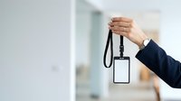 Hand holding blank ID badge with black lanyard in office environment for corporate identity and access control purposes.