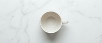 Empty white ceramic cup on marble surface, overhead view, minimalist design for beverage, kitchen, or cafe concepts.