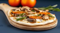Fresh homemade flatbread topped with mushrooms, carrots, rosemary herbs and melted cheese served on wooden cutting board against dark background.