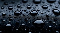 Water drops of various sizes on dark surface create dramatic contrast and texture. Macro photography captures pure liquid beads with surface tension and reflection.
