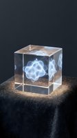 Crystal cube with laser-engraved glowing molecular structure inside, displayed on dark textured surface against black background for scientific and tech applications.