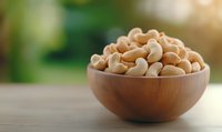 Raw cashew nuts in wooden bowl on rustic table against blurred green natural background, healthy organic snack for vegetarian nutrition.