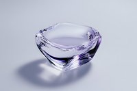 Crystal glass bowl with elegant curved edges casting soft purple reflections and shadows on light background, minimalist luxury decor element.
