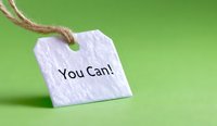 White paper tag with motivational message "You Can!" on green background with natural twine string, shallow depth of field creates soft focus effect.
