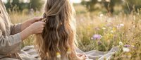 Woman with long wavy hair getting a braid outdoors in a sunny wildflower meadow, warm golden light, natural beauty and summer lifestyle.