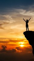 Silhouette of victorious person with raised arms standing on mountain cliff edge against dramatic golden sunset sky with clouds celebrating success and achievement.