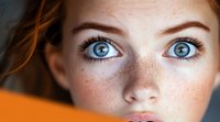 Young Caucasian woman with striking blue eyes and natural freckles looking directly at camera with intense gaze and flawless skin in close-up portrait.