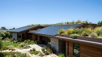 Modern eco-friendly house with living green roof and solar panels surrounded by native landscaping under clear blue sky for sustainable architecture.