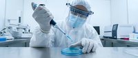 Scientist in protective suit conducting laboratory research with pipette and petri dish in modern medical facility for scientific analysis and testing.