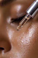 Closeup of serum dropper with water droplet above glowing hydrated skin, showing skincare product application with dewy moisture effect and radiant complexion.