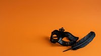 Black masquerade mask with feather on orange background, isolated for costume design, party invitations, and event marketing materials.