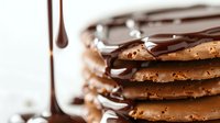Stacked chocolate chip cookies with dripping melted dark chocolate sauce creating indulgent dessert composition. Fresh baked treats with gooey topping.