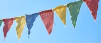 Colorful triangular prayer flags hanging against clear blue sky creating festive outdoor celebration atmosphere for parties and cultural events.