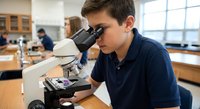 Young male student using microscope in science laboratory classroom conducting research experiment for educational study.