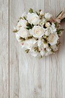 Elegant white rose bridal bouquet with satin ribbon on rustic wooden background, perfect for wedding photography and floral design inspiration.