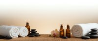 Spa wellness setup with essential oil bottles, hot stones, rolled towels and candles on bamboo mat creating relaxing atmosphere for massage therapy.
