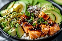Fresh salmon poke bowl with sliced avocado, white rice, green onions and black sesame seeds in teriyaki sauce, close up view of Asian cuisine.