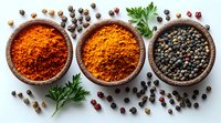 Aromatic spices in wooden bowls - red chili powder, turmeric powder and black peppercorns with fresh parsley leaves scattered on white background.