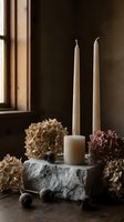 Marble candle holder with two tall cream taper candles surrounded by dried hydrangea flowers and spheres, positioned near a window with natural light for home decor and styling.