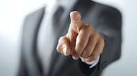 Businessman in formal suit pointing finger directly at viewer, conveying leadership, choice, or accusation in professional corporate setting.