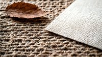 Brown autumn leaf on natural burlap textile background with linen fabric piece, showing detailed woven texture and organic materials in warm tones.