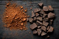 Dark chocolate pieces and cocoa powder scattered on black rustic wooden background, top view composition for confectionery and baking designs.