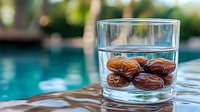 Fresh dates soaking in clear water glass with swimming pool and natural bokeh background, healthy organic snack for breaking fast during Ramadan.