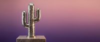 Golden metallic cactus sculpture on wooden base against pink purple gradient background for modern home decor and desert themed interior design concepts.