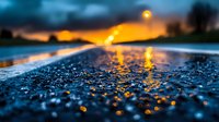 Dramatic wet asphalt road after rain with golden sunset reflection in water drops, street lights glowing in dusk creating atmospheric moody scene.