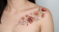 Delicate watercolor poppy flowers tattoo on woman shoulder featuring orange and red blooms with flowing stems in artistic botanical design.