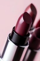 Deep burgundy lipstick in metallic silver tube against soft pink background with dramatic shadow creating luxury cosmetic mood for beauty advertising.