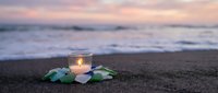 Glowing candle with sea glass on sandy beach at sunset creating peaceful meditation atmosphere for relaxation and mindfulness practices.